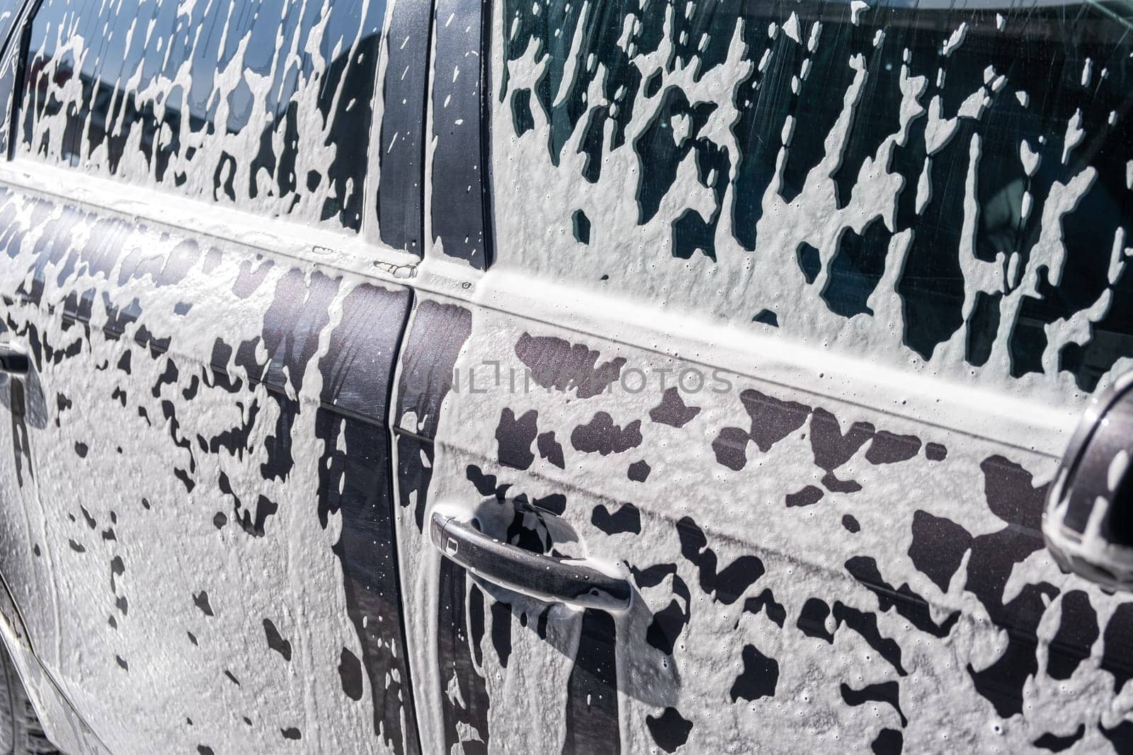 Foamy car at car wash, with tire, wheel, and hood covered in suds by AnatoliiFoto