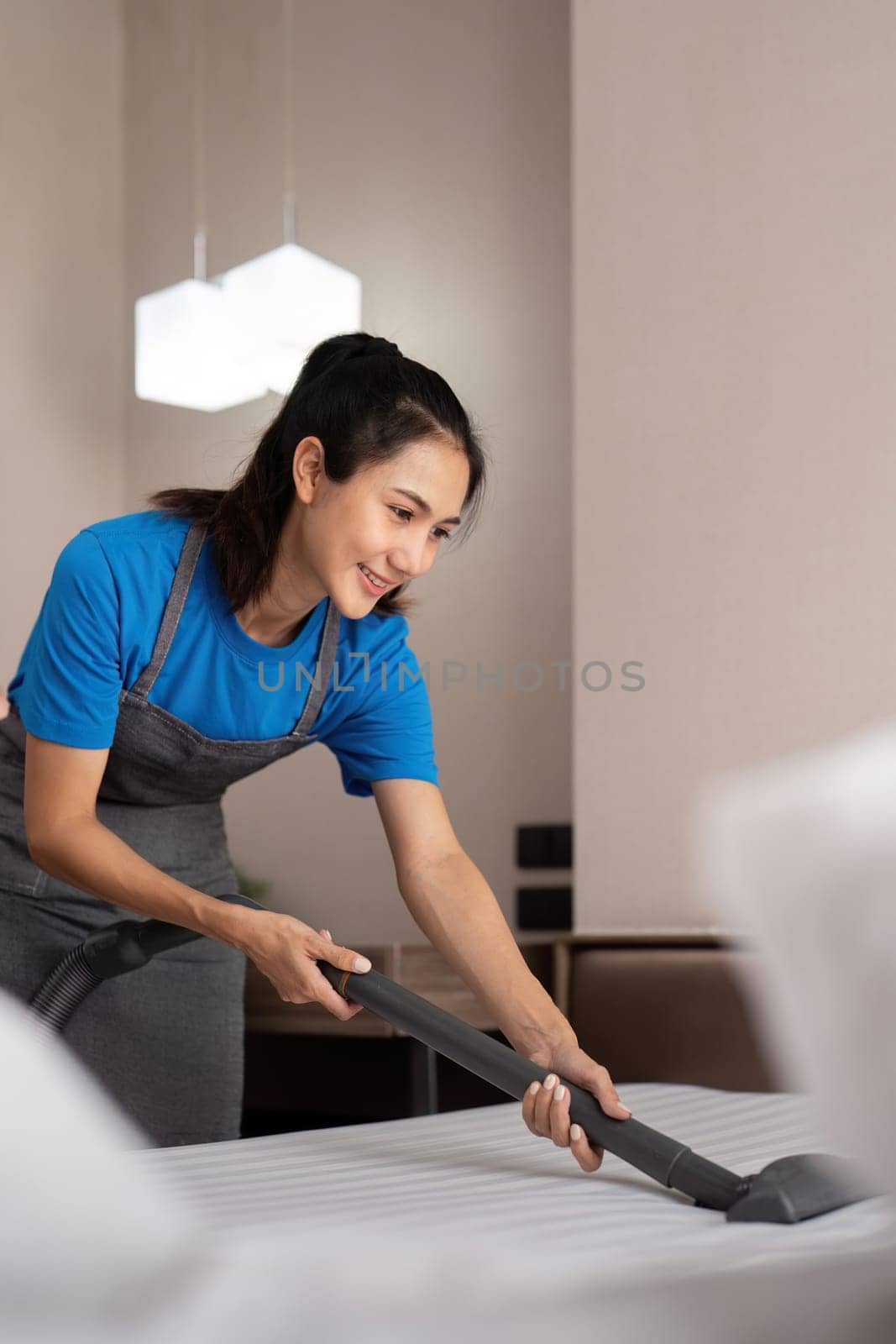 Cleaning service employee removing dirt from with professional equipment. Female housekeeper cleaning the mattress on the bed with vacuum cleaner by nateemee