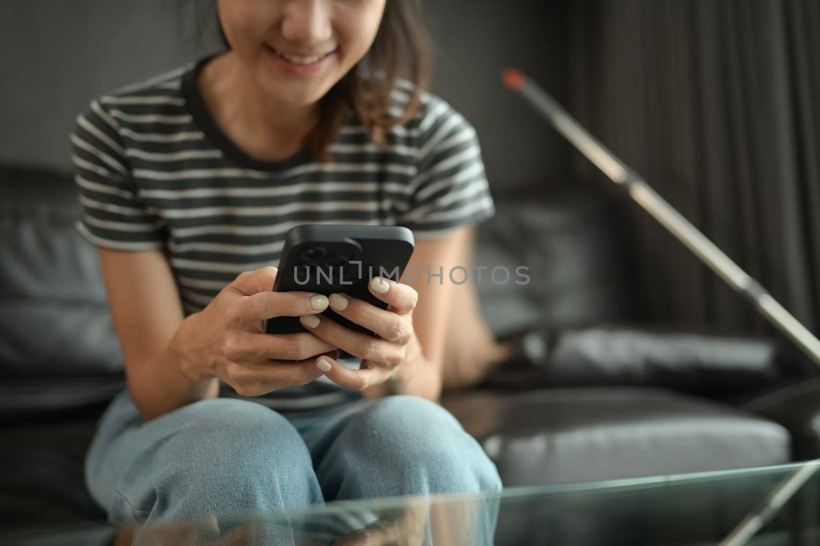 Cropped shot of smiling young woman relaxing on couch and using mobile phone.