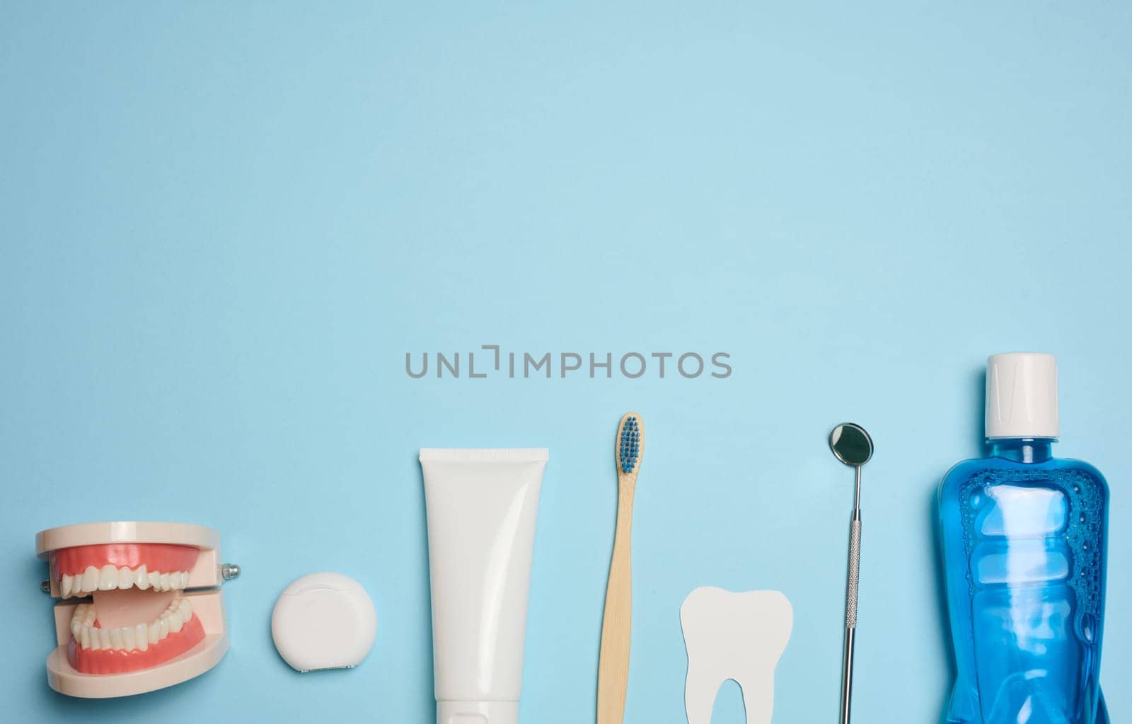 Mouthwash, toothpaste tube, dental floss and medical mirror on a blue background, oral hygiene. Top view