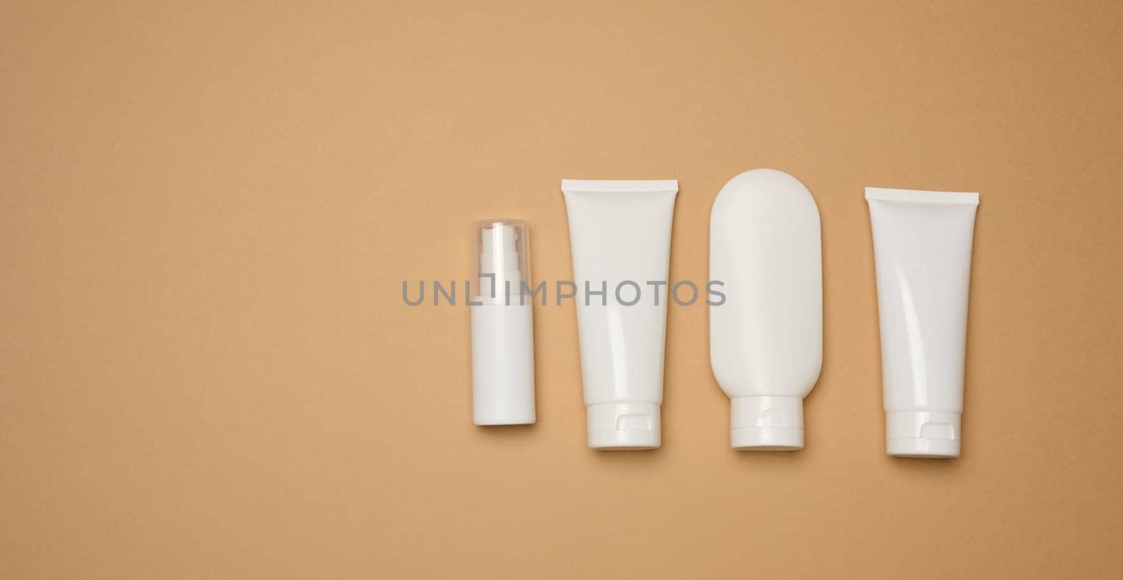 White plastic tubes, jars, and containers for cosmetic products on a brown background, advertising and branding of products