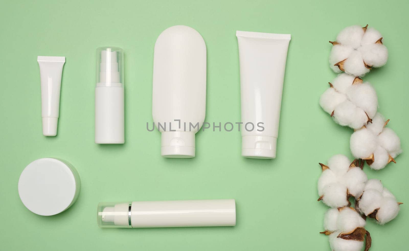 White plastic tubes, jars, and containers for cosmetic products on a green background, advertising and branding of products