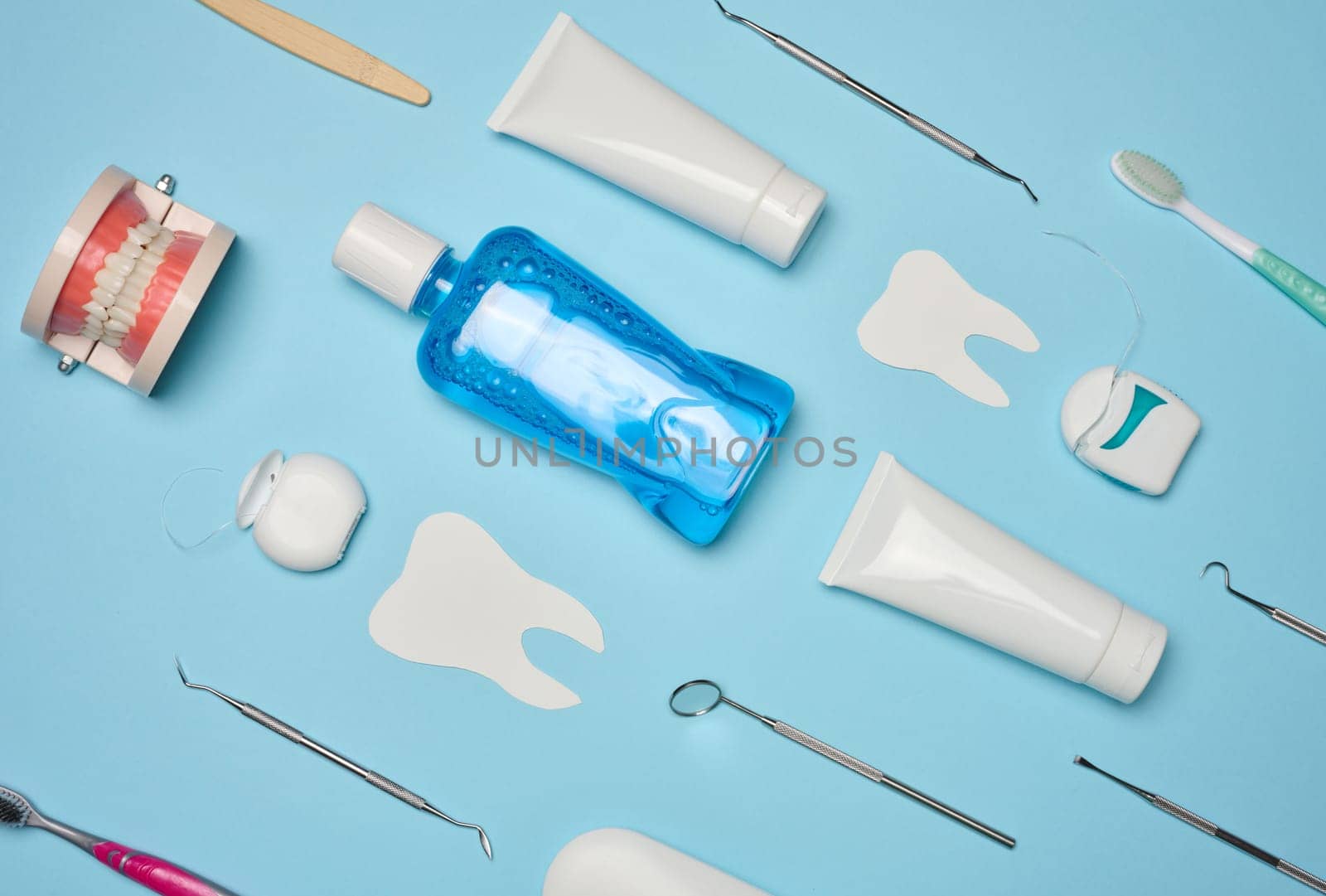 Mouthwash, toothpaste tube, dental floss and medical mirror on a blue background, oral hygiene. Top view