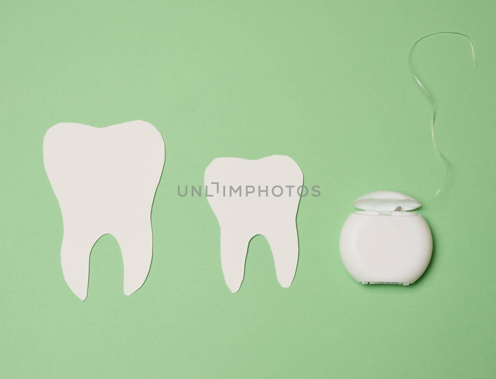 Dental floss and paper teeth on green background, oral hygiene by ndanko