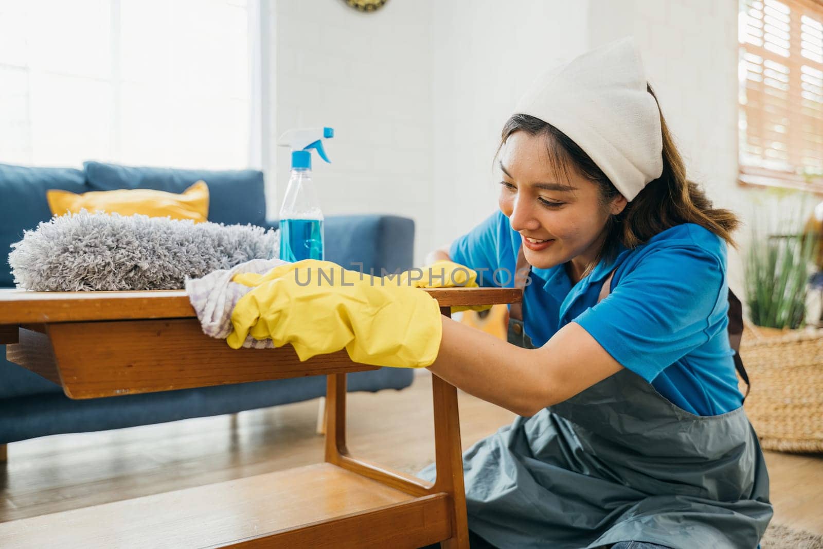 With a smile a diligent woman in yellow gloves wipes and cleans her living room table. Her commitment to home cleanliness and hygiene is evident in her routine cleaning tasks. maid clean desk. by Sorapop