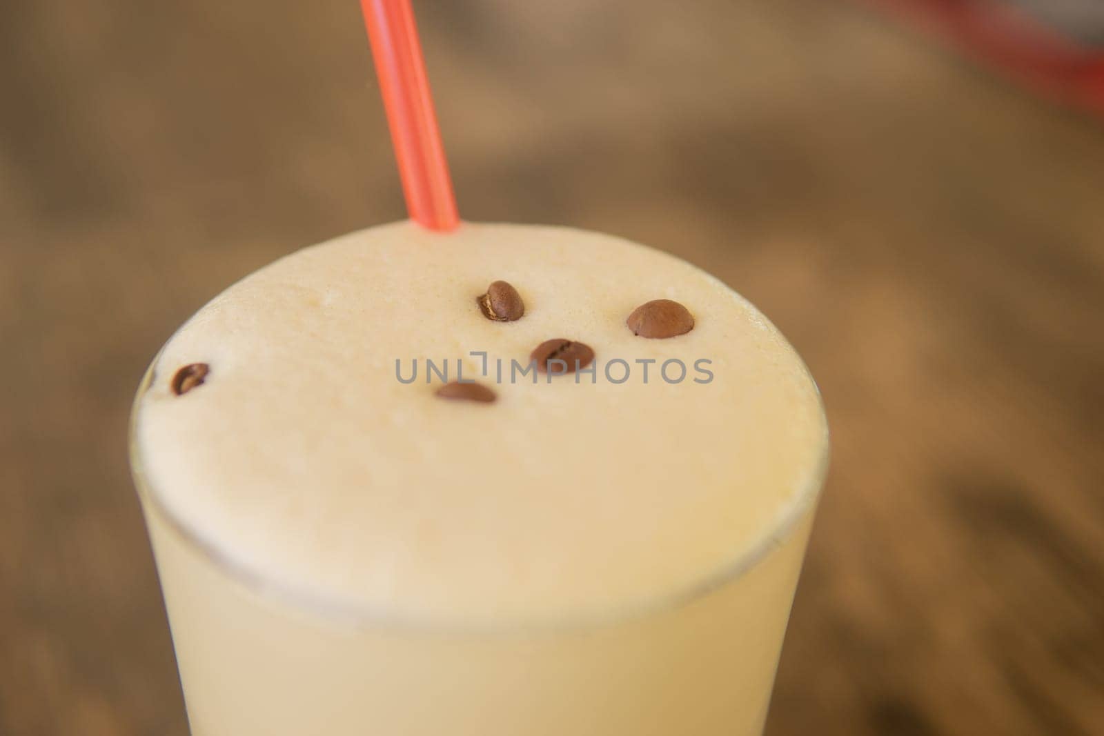 A cold coffee cocktail in a clear glass with a straw on a wooden bar counter.