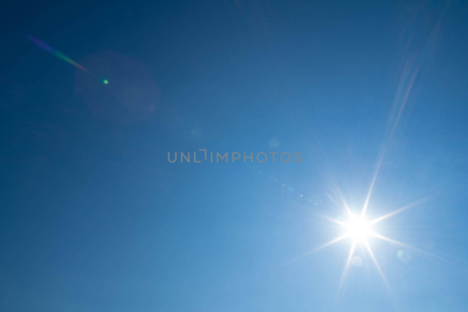 Sharp sunbeams on a cloudless day in summer and holiday time. Clear blue sky background.