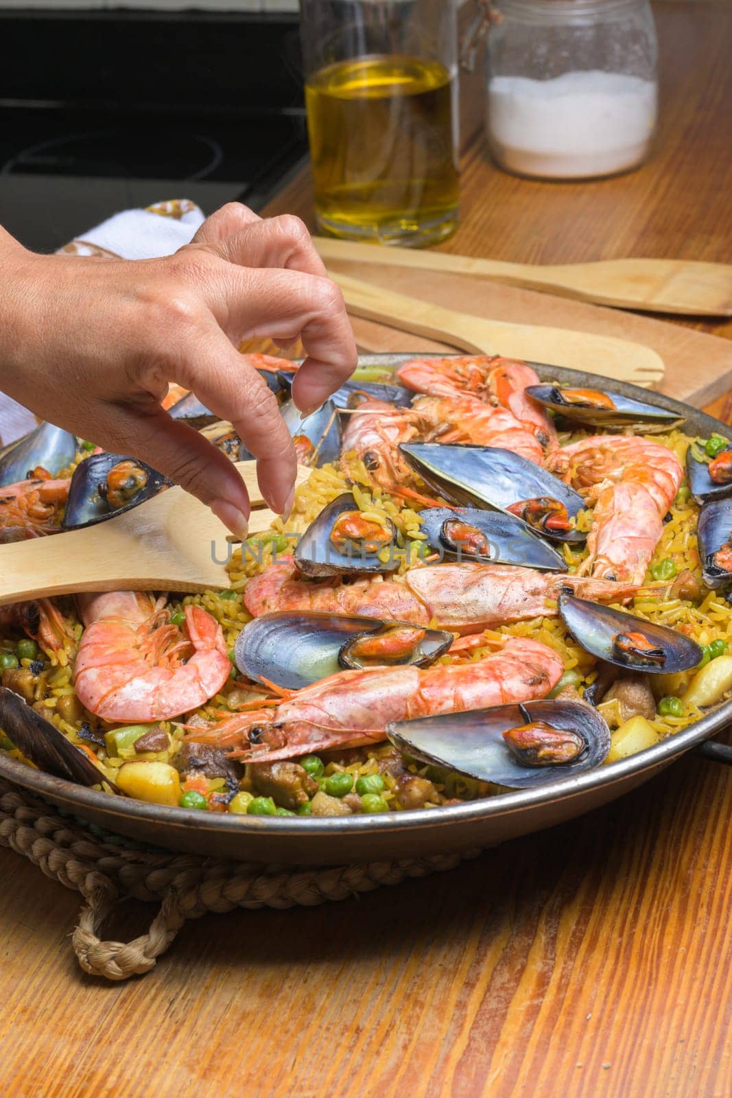 A hand serving seafood paella with prawns and mussels using a wooden spatula, typical Spanish cuisine, Majorca, Balearic Islands, Spain,