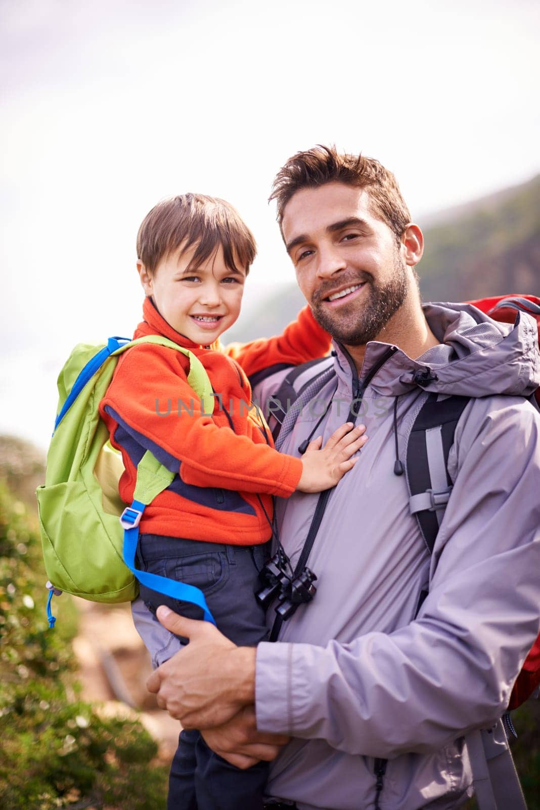 Father, child and hiking portrait with smile, backpack and travel with happy and support in nature. Kid, adventure and mountain with love, trust and bonding with family and journey for holiday.