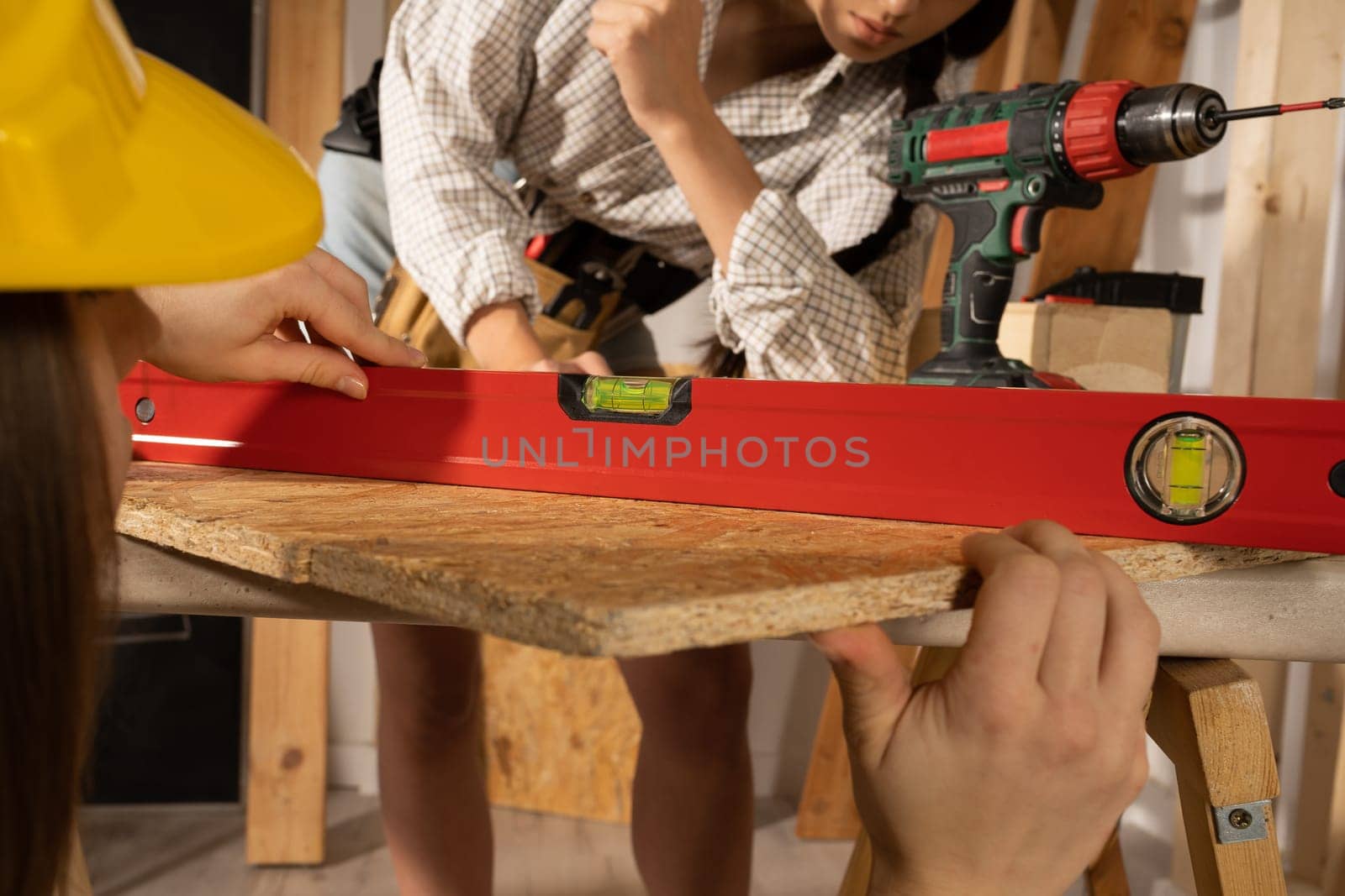 The blonde puts a red spirit level to the table top and the brunette checks if the indications are correct.