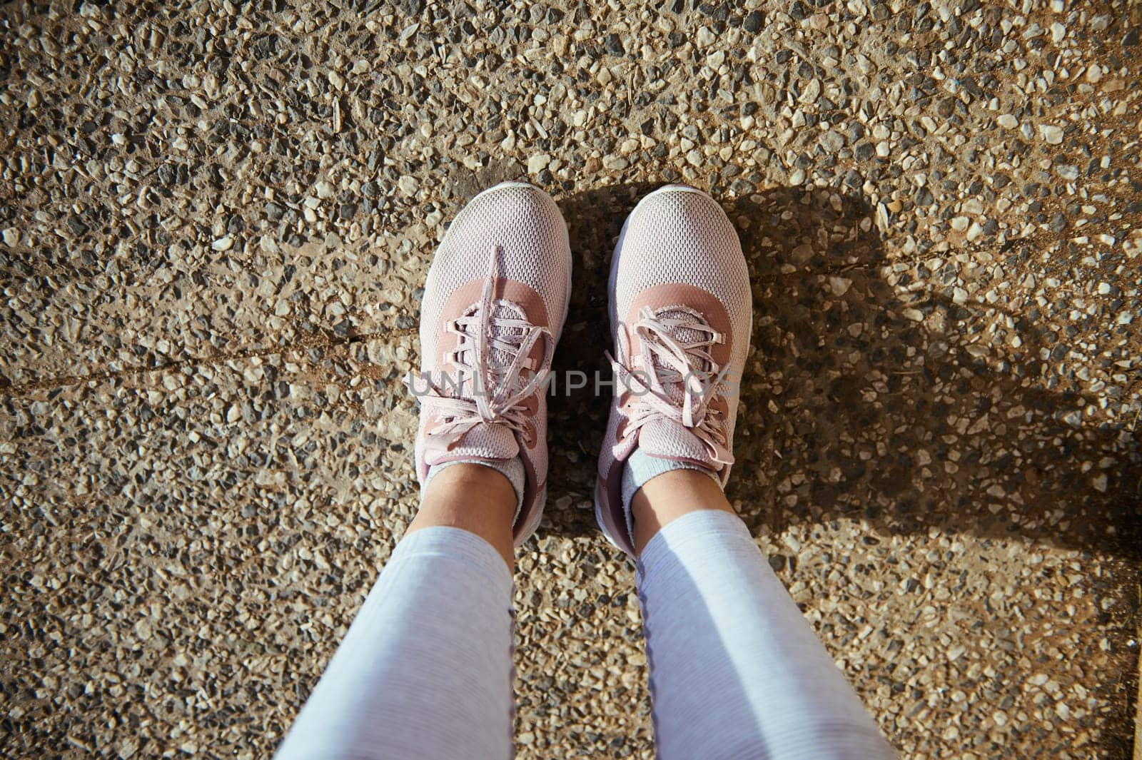 Sportswoman point of view. Legs and feet of female athlete in stylish running sports shoes, pink sneakers on the asphalt by artgf