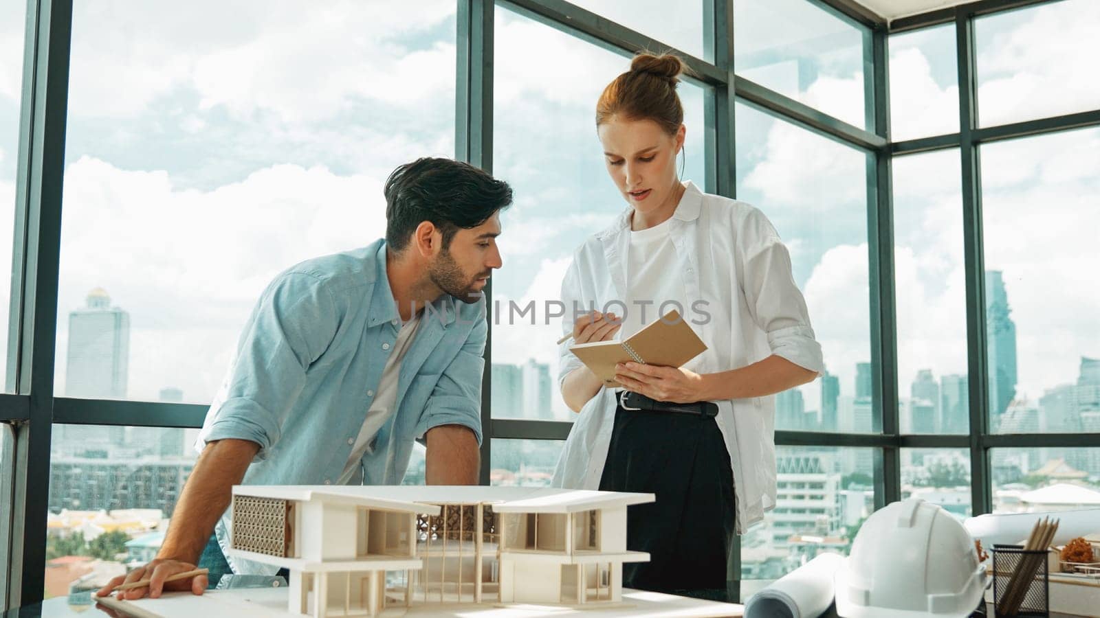 Skilled architect engineer team discussion about house model construction. Smart interior designer sharing, talking about building design while beautiful coworker taking a note. Design. Tracery