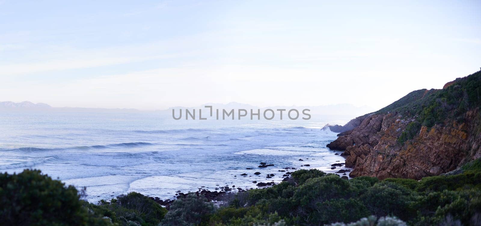 Ocean, nature and mountain in environment outdoor for vacation, holiday and travel in South Africa. Sea, water and waves with landscape, blue sky and mockup space in the countryside at coastline.