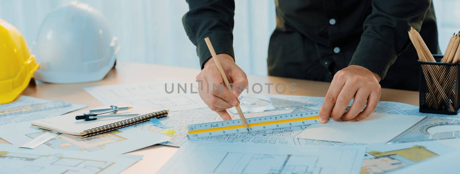 Professional engineer measuring the blueprint. Professional engineer working architectural project at studio on a table with yellow helmet and architectural equipment scatter around. Delineation.