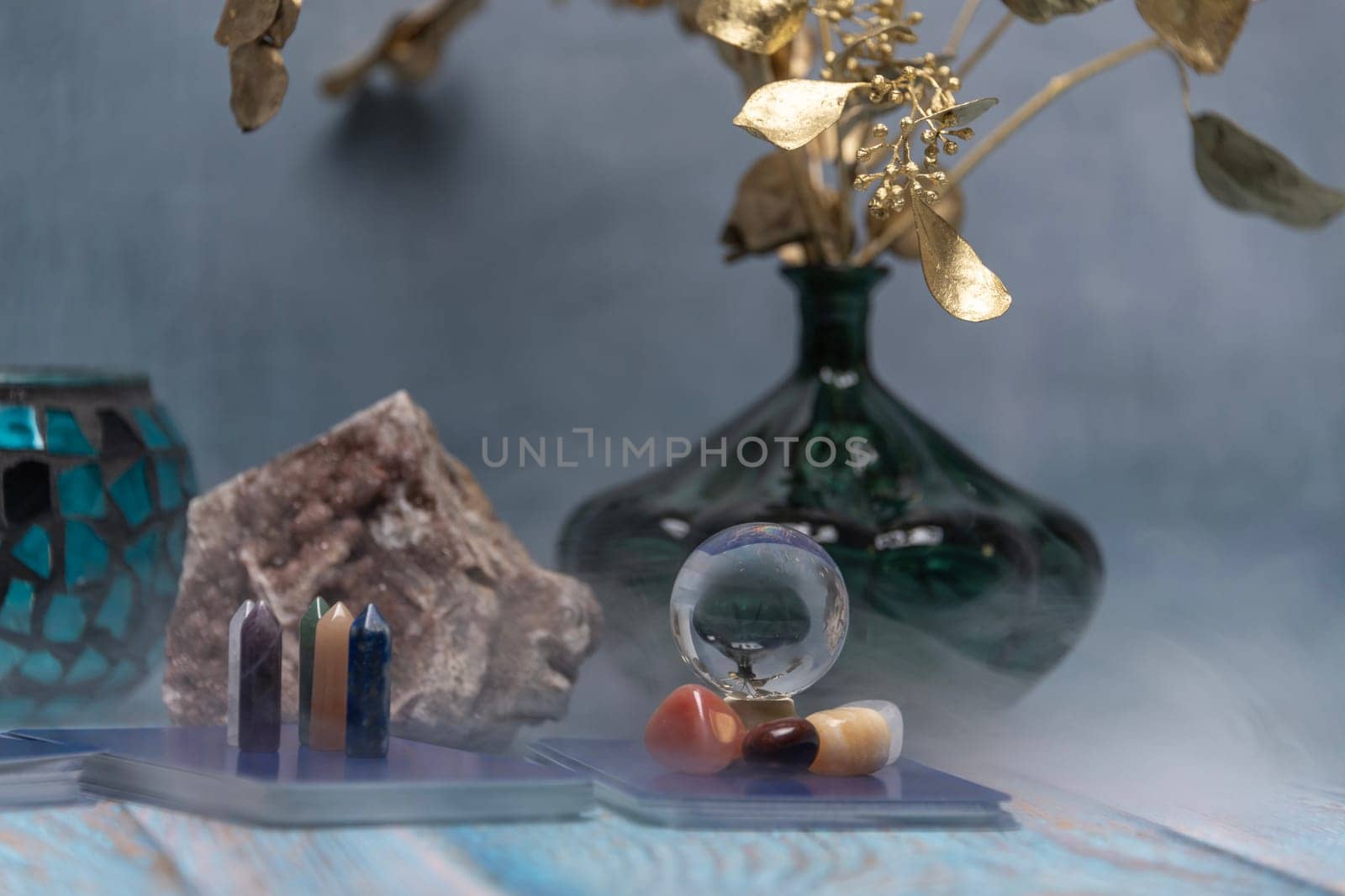 A serene tarot card reading space with assorted healing crystals, a candle lantern, and a geode on a weathered wooden surface. by jbruiz78