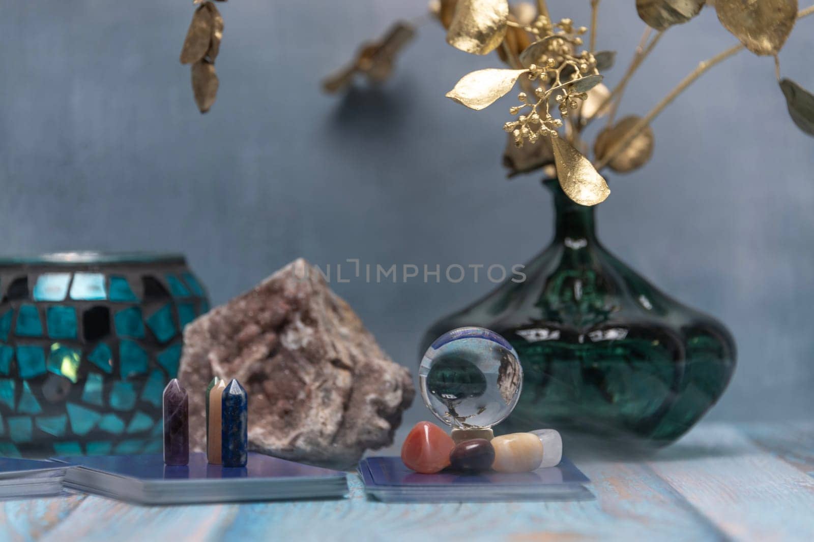A serene tarot card reading space with assorted healing crystals, a candle lantern, and a geode on a weathered wooden surface. by jbruiz78
