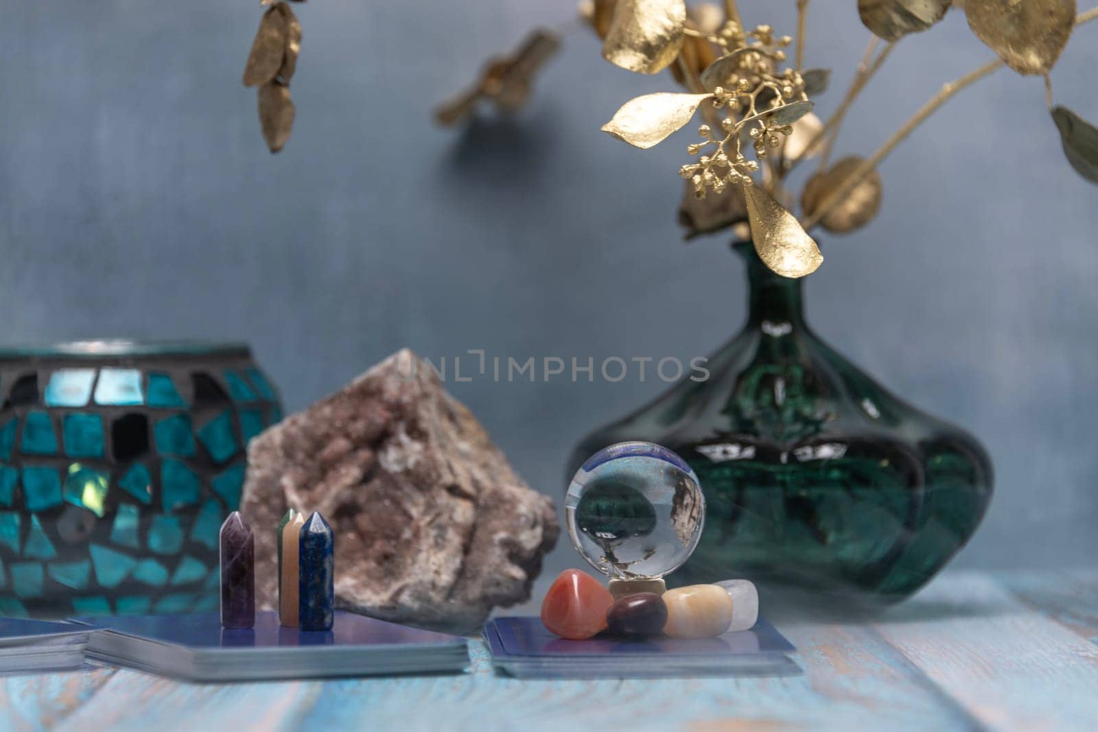 A serene tarot card reading space with assorted healing crystals, a candle lantern, and a geode on a weathered wooden surface