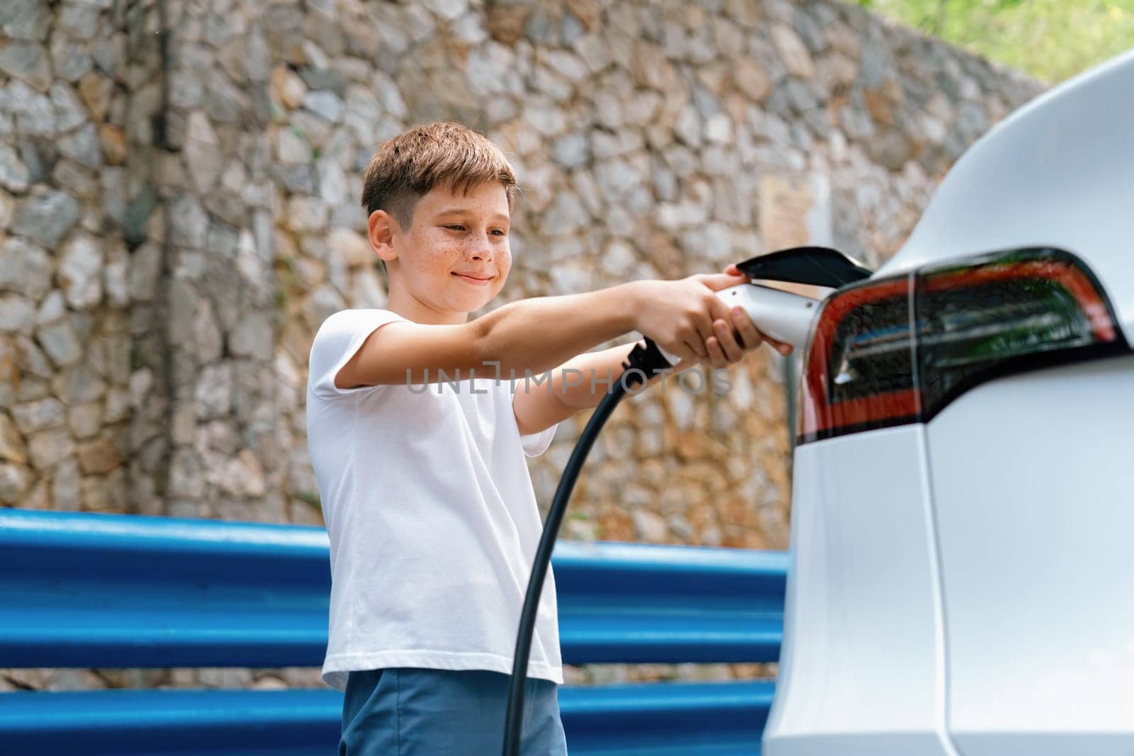 Little boy recharging eco-friendly electric car from EV charging station. EV car road trip travel concept for alternative transportation powered by clean renewable and sustainable energy. Perpetual