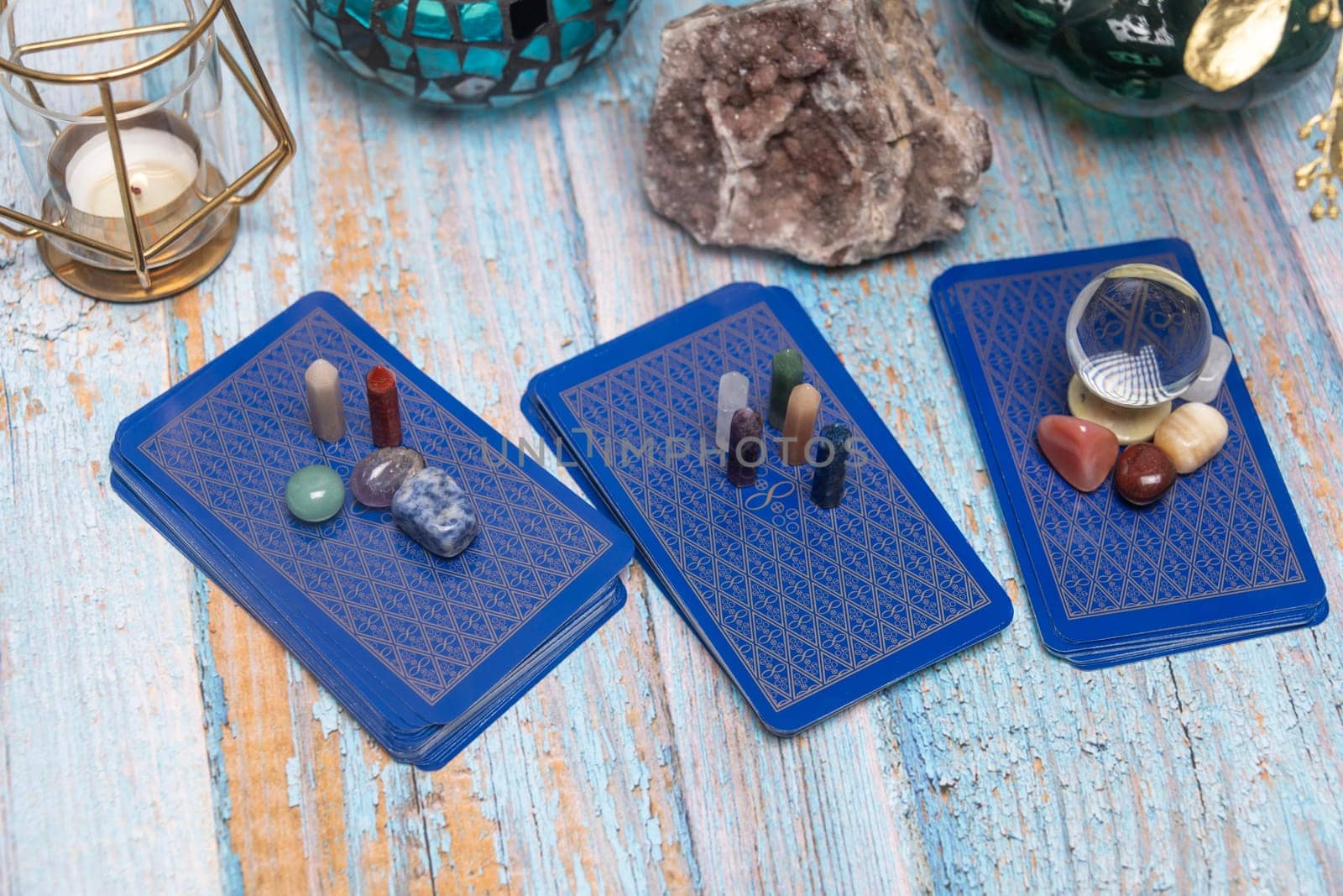 A serene tarot card reading space with assorted healing crystals, a candle lantern, and a geode on a weathered wooden surface