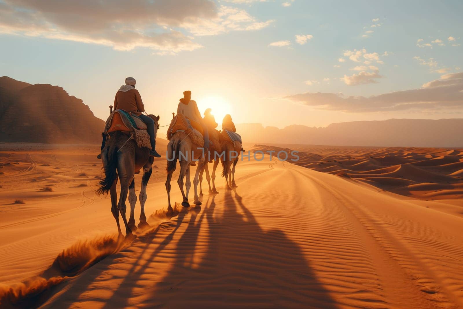 A group of travelers are riding pack camels through the desert landscape as the sun sets behind the aeolian landforms, creating a beautiful dusk sky