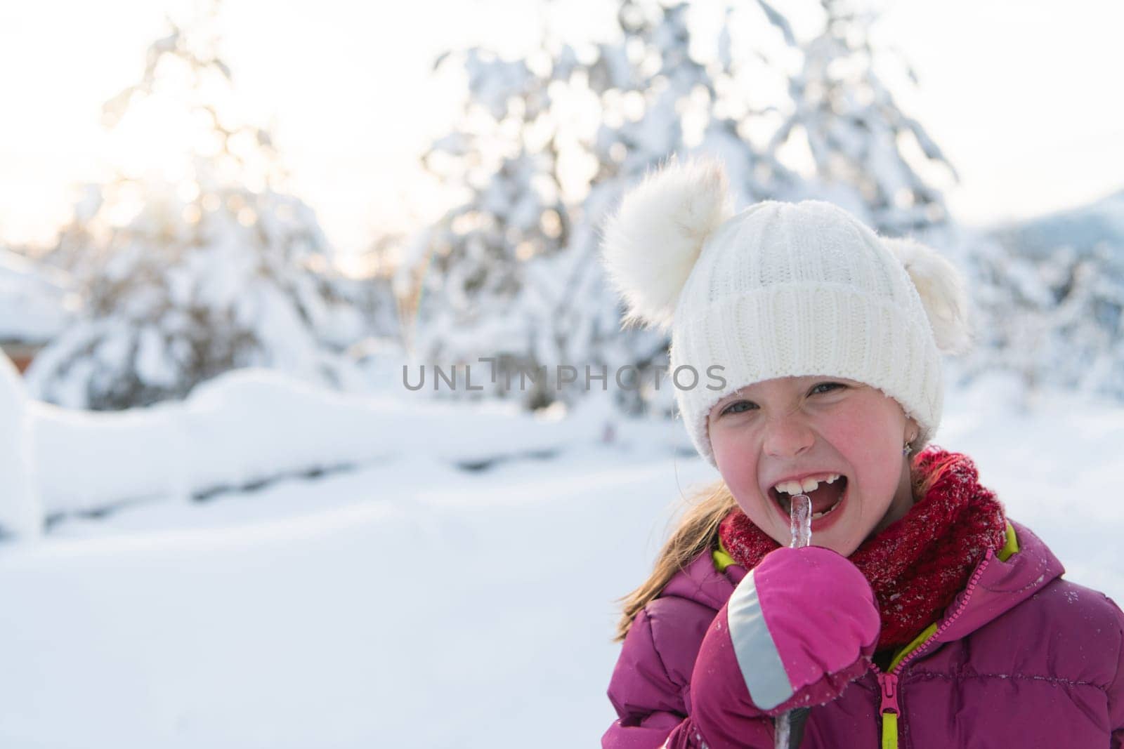 Cute little girl while eating icicle on beautiful winter day.