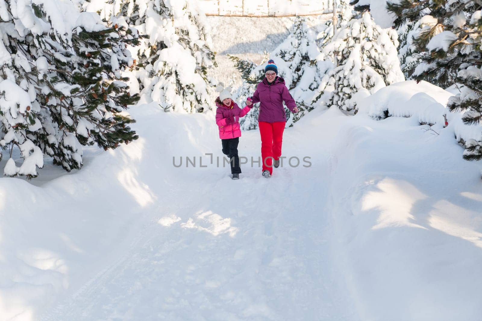 A mother and daughter as they dash along a serene snowy path, embracing the tranquil beauty of their winter mountain getaway.