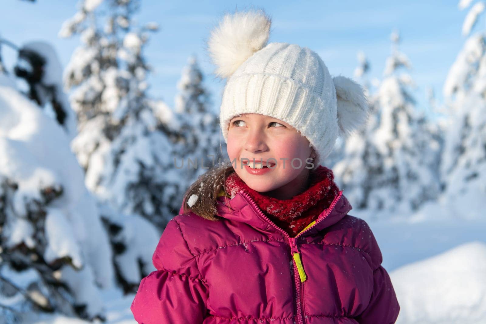 A radiant girl smiles against a backdrop of snow-capped mountains, the sun illuminating her joyful expression.