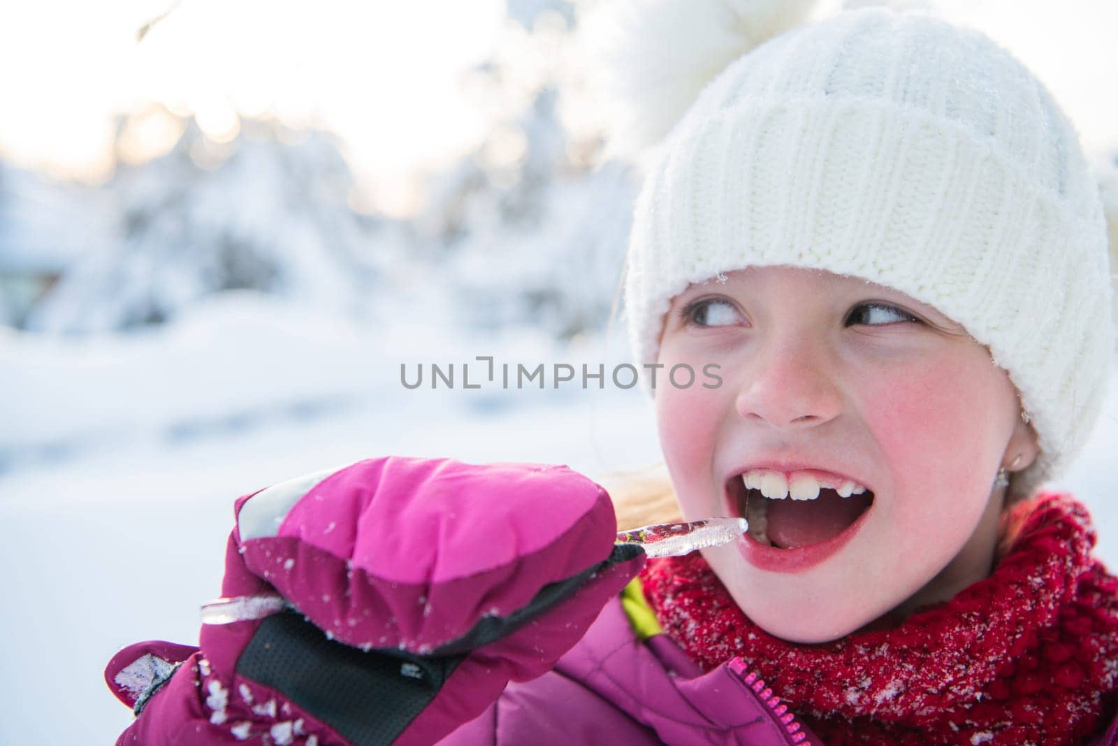 Cute little girl while eating icicle on beautiful winter day.