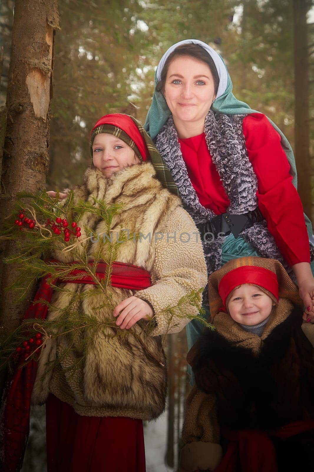 Family with mother, teenage girl, and little daughter dressed in stylized medieval peasant clothing in winter forest. Woman and her daughters pose for fairytale photoshoot in nature on a cold day