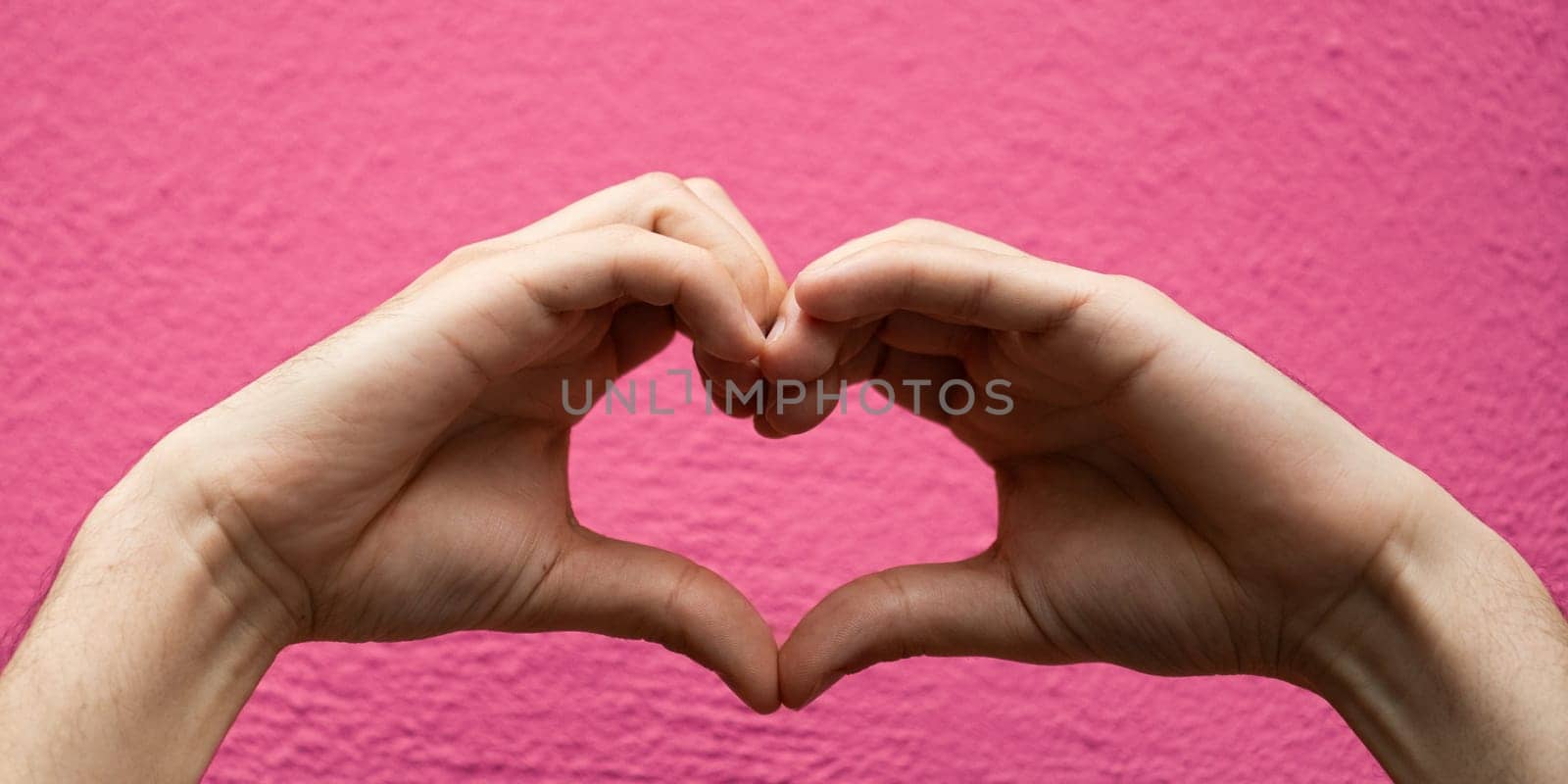 Hands forming a heart shape isolated on pink background.