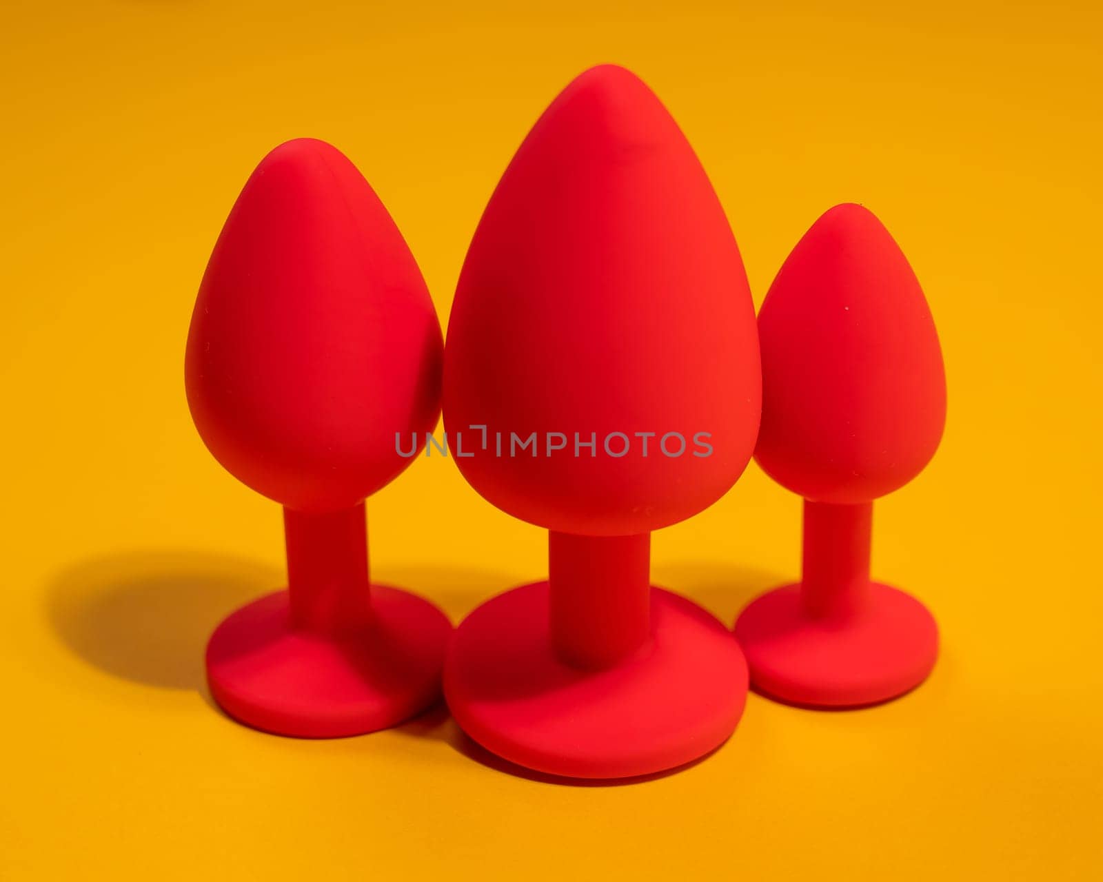 Three size silicone red butt plugs on an orange background. by mrwed54