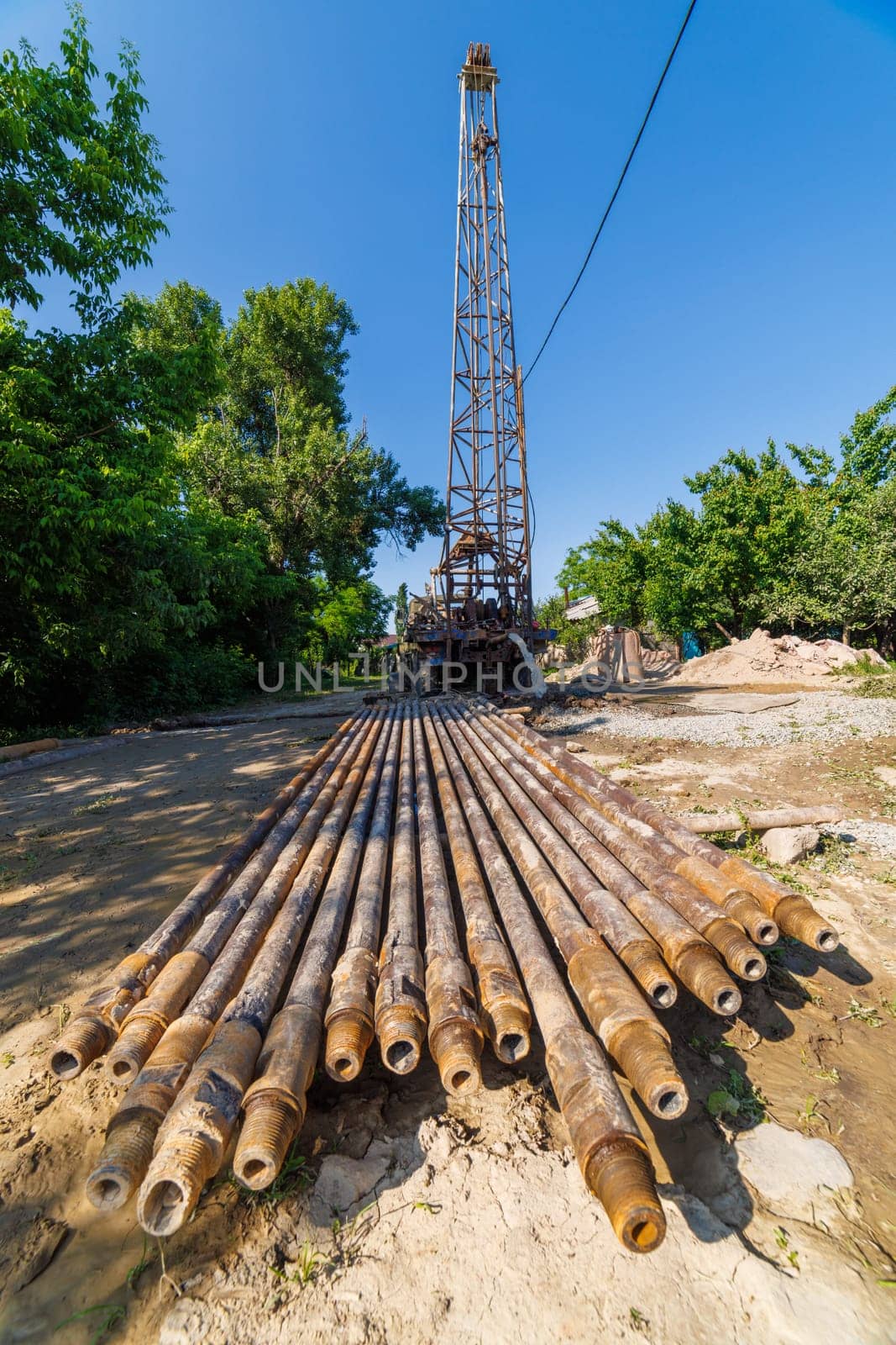 extension drilling rods in front of old water pump truck extracts water from a hole in the ground at sunny summer day, surrounded by a natural landscape with trees, plants, and soil. Ultra-wide angle.