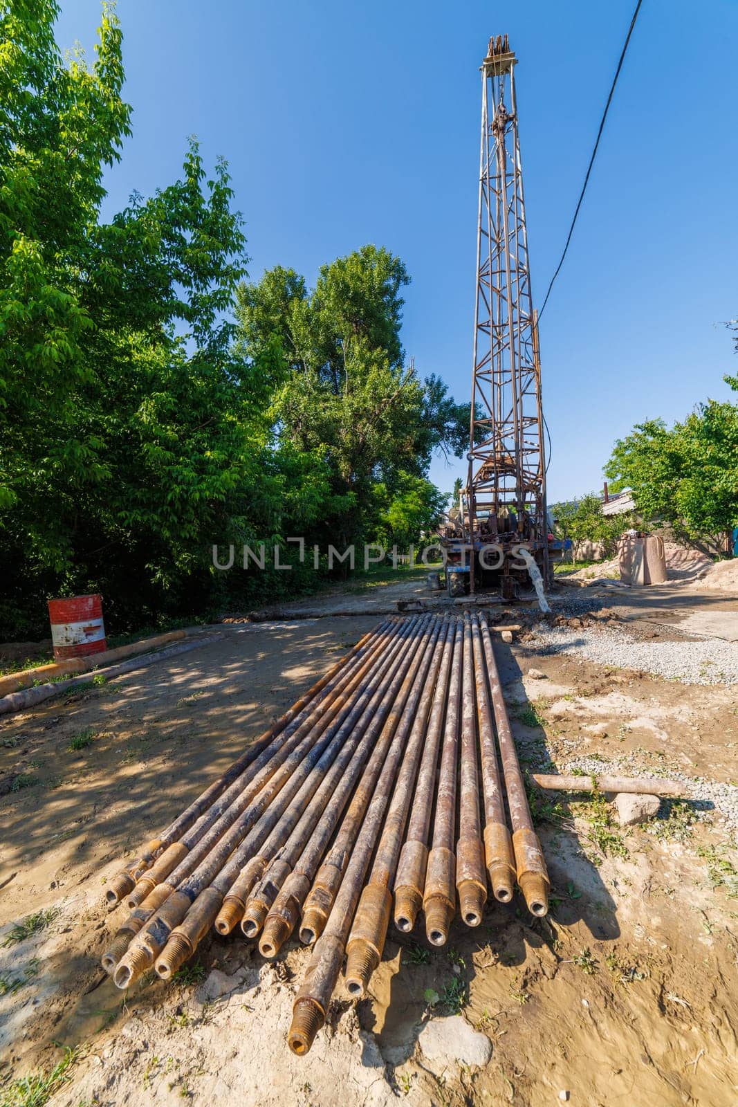 extension drilling rods in front of old water pump truck extracts water from a hole in the ground at sunny summer day, surrounded by a natural landscape with trees, plants, and soil. Ultra-wide angle.