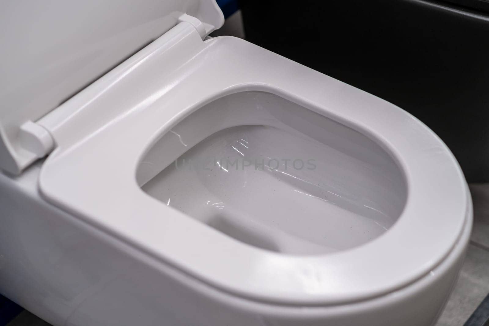 A closeup image of a white toilet in a bathroom. The toilet seat is made of plastic and the fixture is a rectangle shape. It is a composite material with metal parts