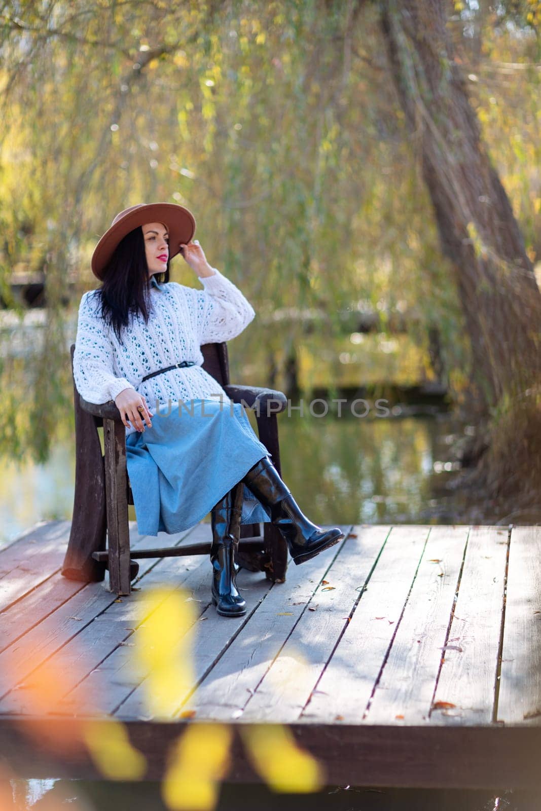 Autumn lake woman. She sits by a pond on a wooden pier in autumn and admires nature. The concept of tourism, weekends outside the city. by Matiunina