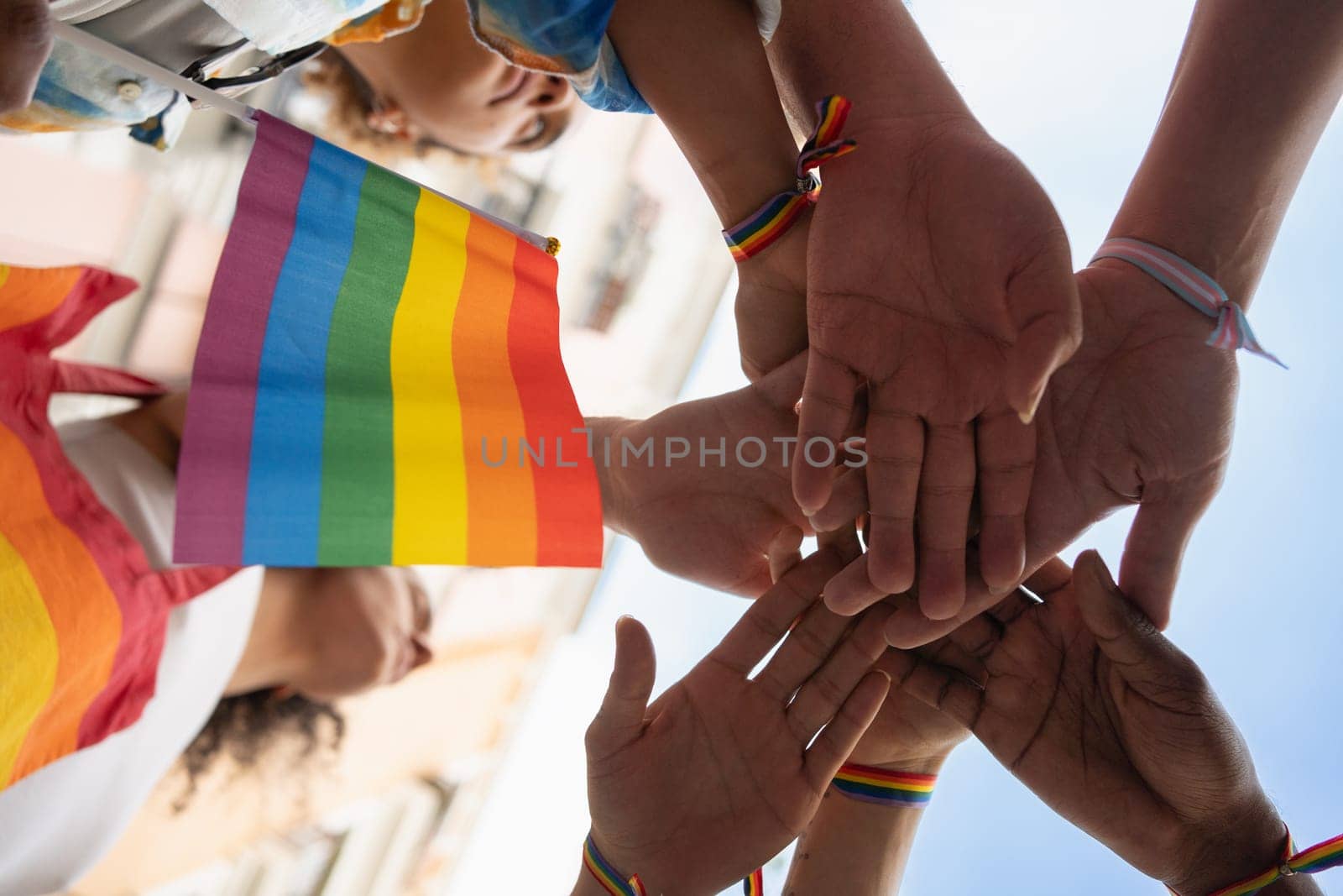 A group of people are holding hands and a rainbow flag. Scene is one of unity and support for the LGBTQ community.