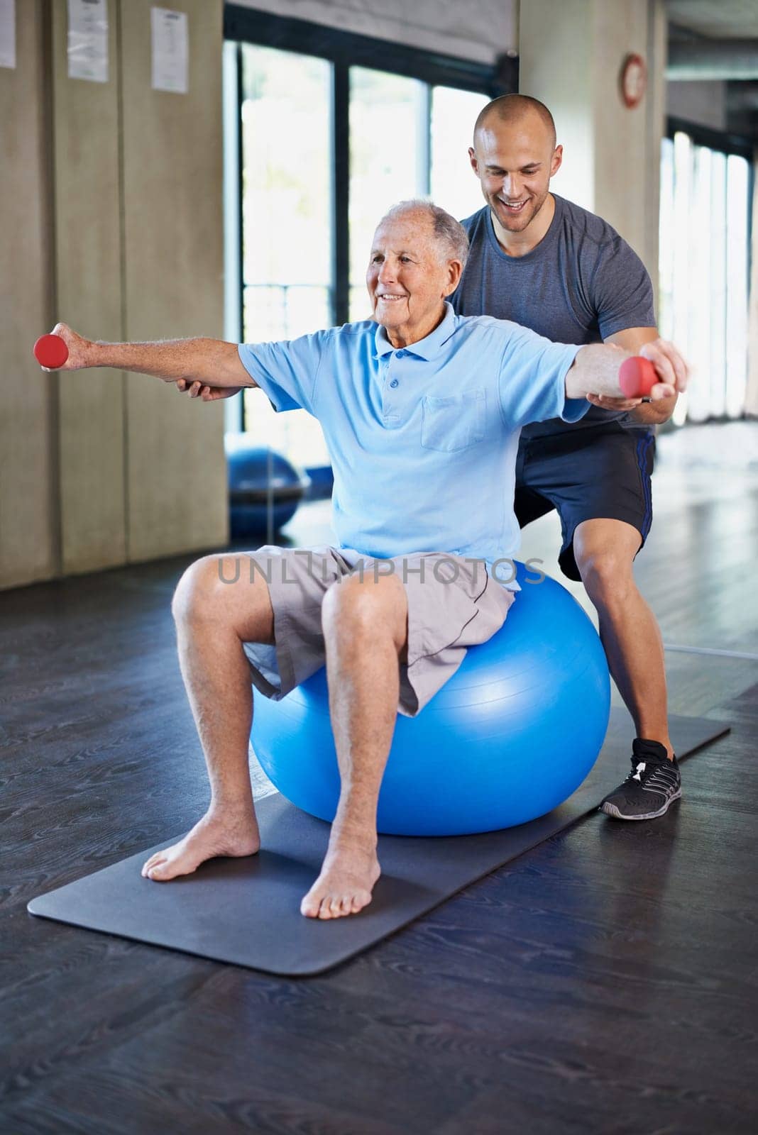 Physiotherapist, helping and senior man with dumbbell, training and elderly support for care. Men, gym and exercise for health, wellness and coaching with yoga ball for mature rehab and wellbeing by YuriArcurs