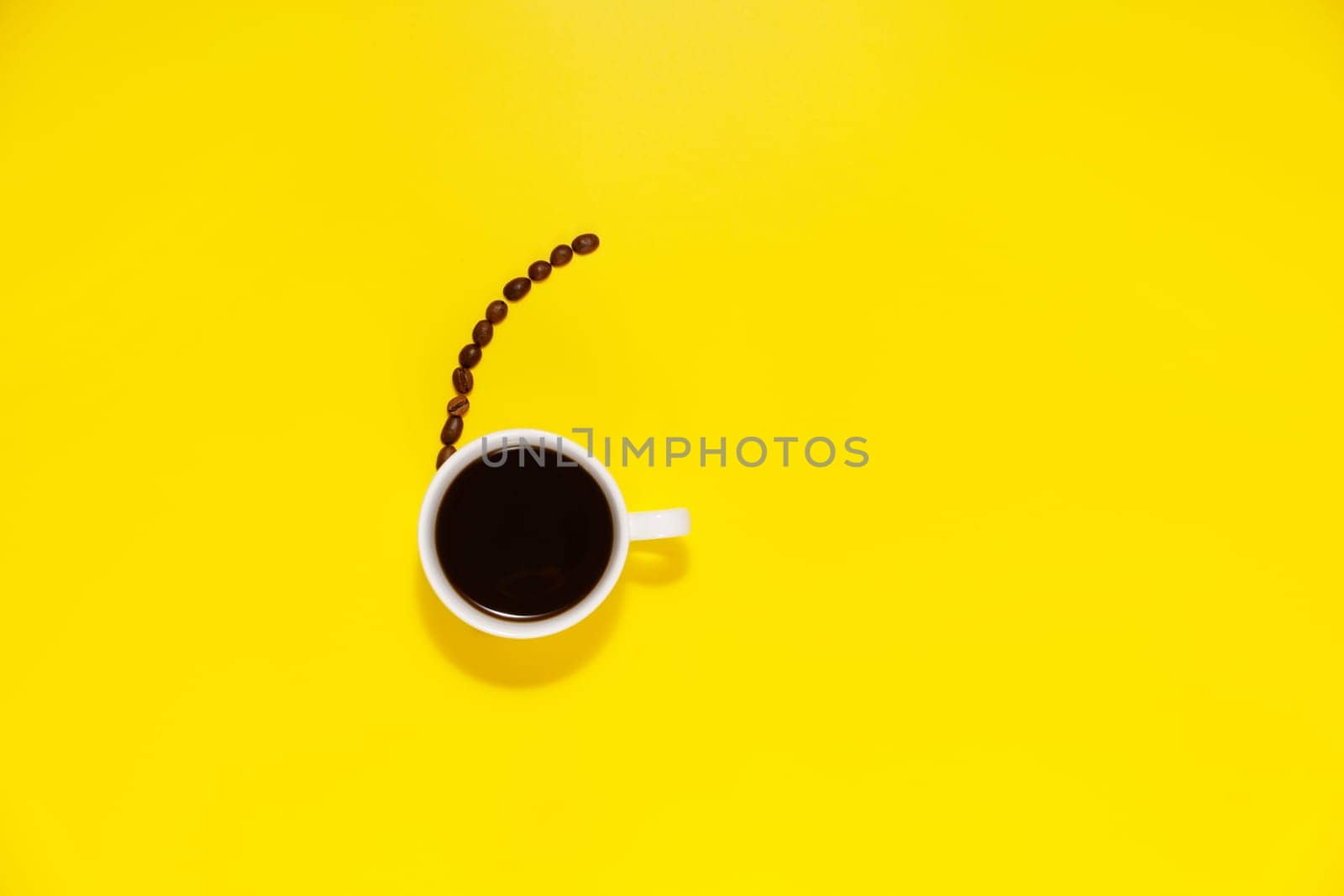 Cup of coffee and coffee bean on a yellow background, with space for copy text.