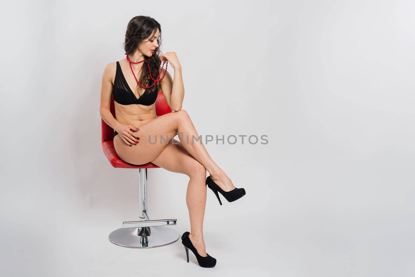 Cute brunette female model posing, wearing black and red underwear in a white studio