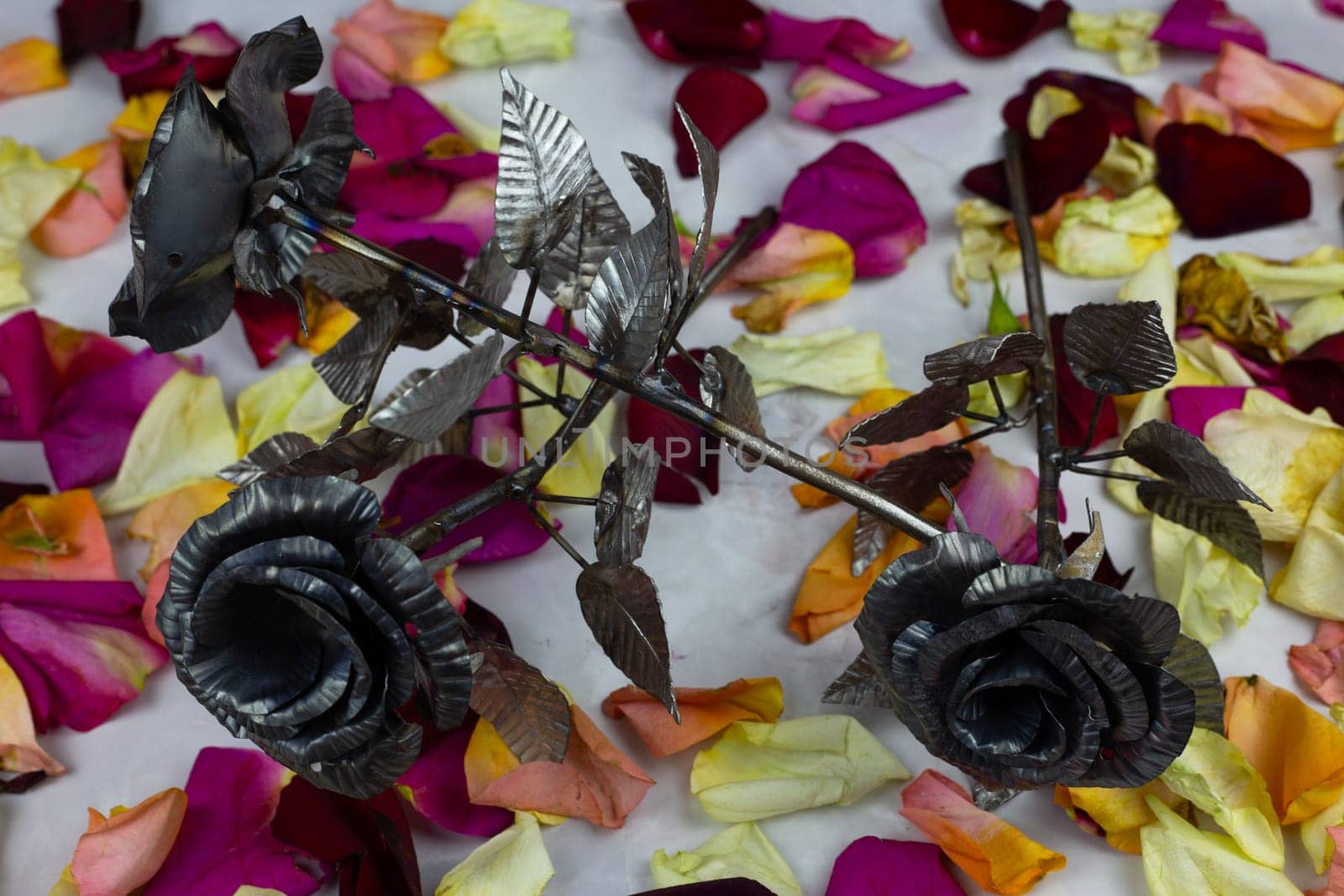 Metal roses as holiday gift, artificial flowers against the background of real rose petals
