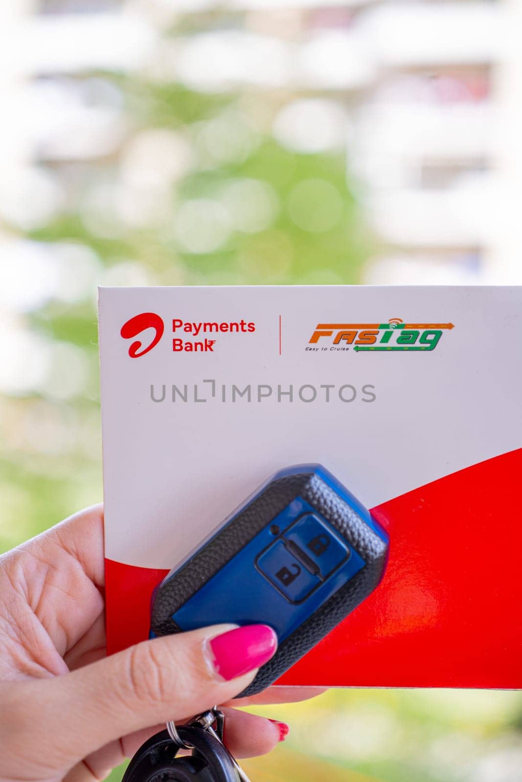 Delhi, India - 27th Mar 2024: Woman holding Airtel Payment bank Fastag with car key showing the new payment method from NHAI national highway authority of India for Toll