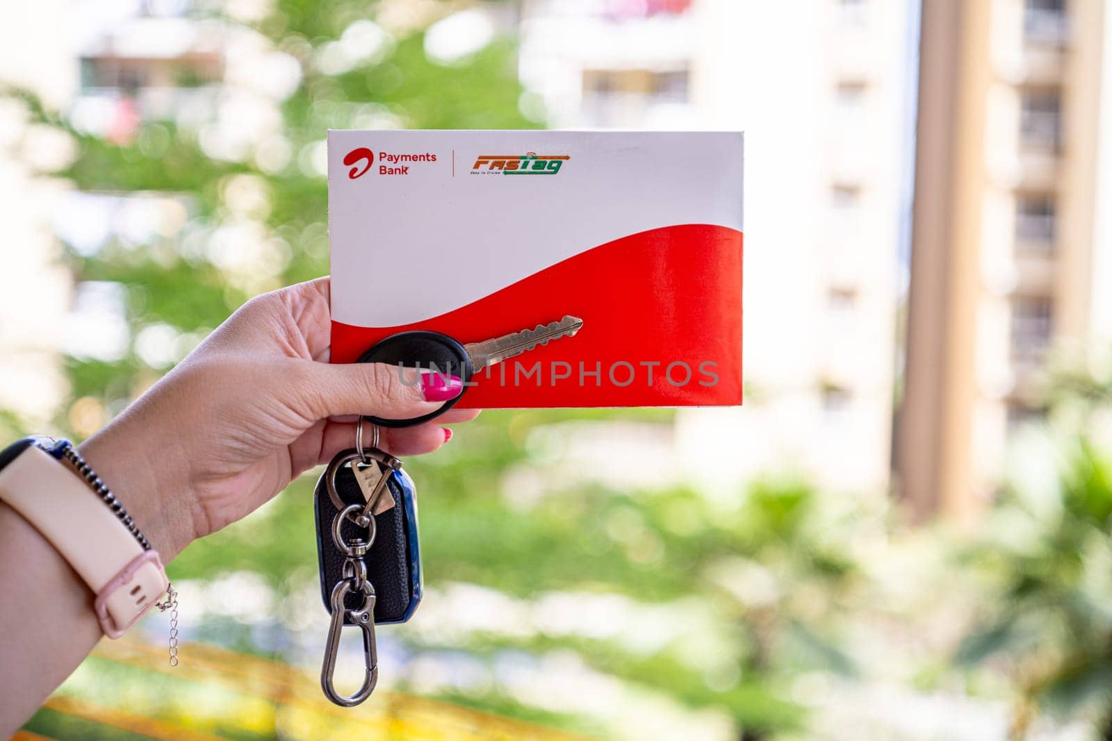 Delhi, India - 27th Mar 2024: Woman holding Airtel Payment bank Fastag with car key showing the new payment method from NHAI national highway authority of India for Toll