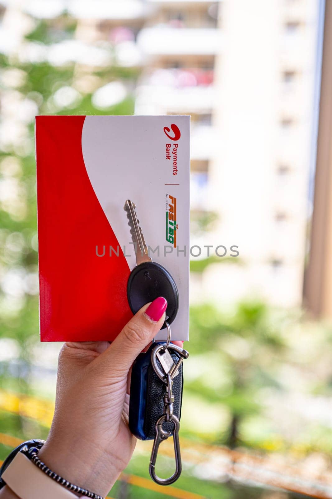 Delhi, India - 27th Mar 2024: Woman holding Airtel Payment bank Fastag with car key showing the new payment method from NHAI national highway authority of India for Toll