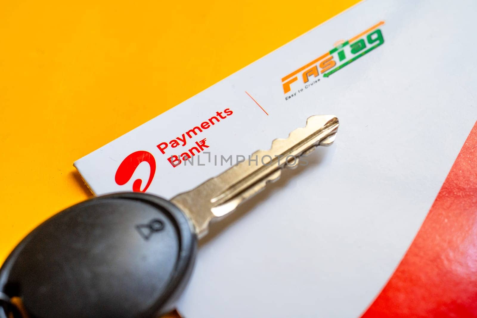 Delhi, India - 27th Mar 2024: Close up shot of Airtel Payment bank Fastag and car key placed on yellow table showing the RFID payment by NHAI