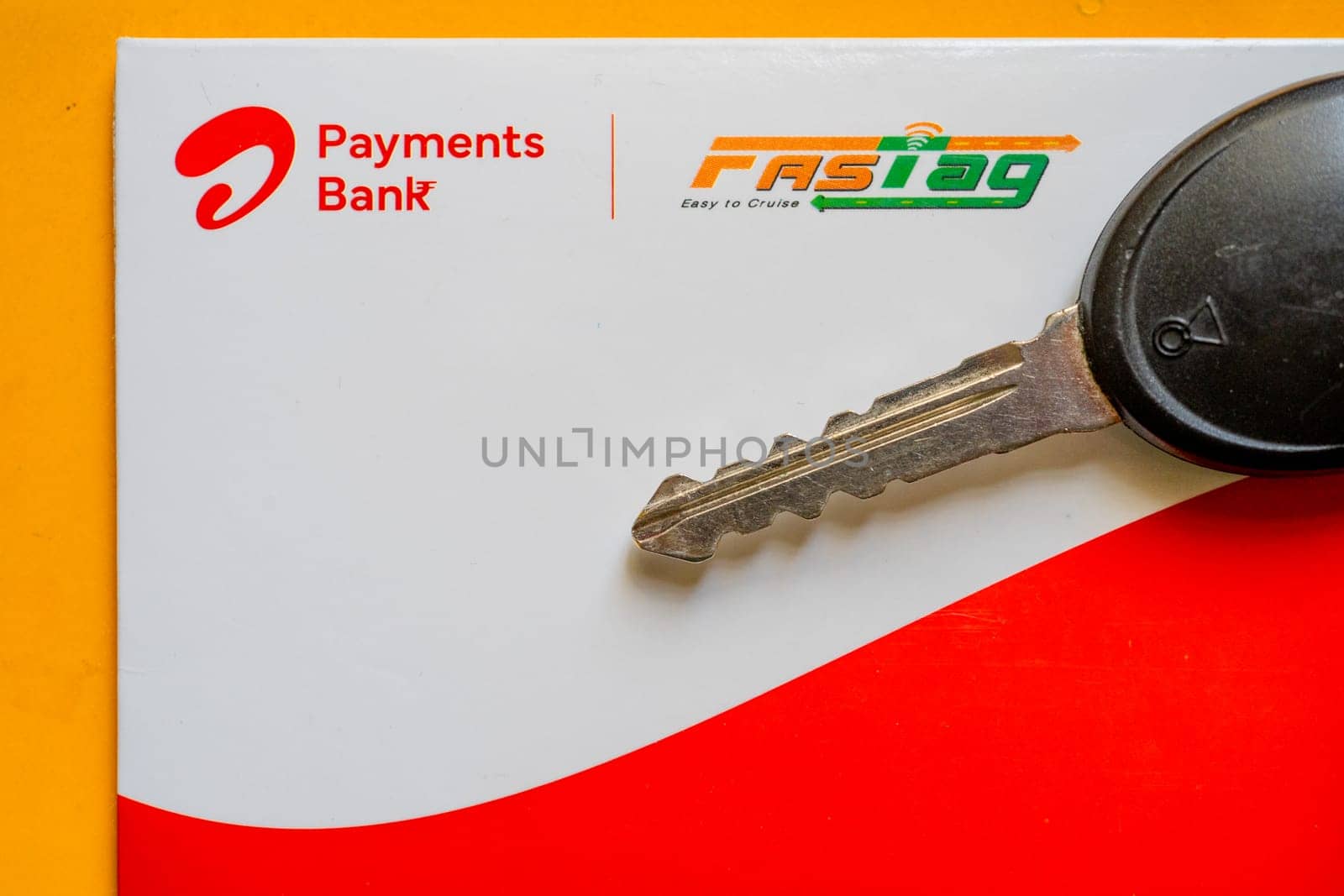 Delhi, India - 27th Mar 2024: Close up shot of Airtel Payment bank Fastag and car key placed on yellow table showing the RFID payment by NHAI