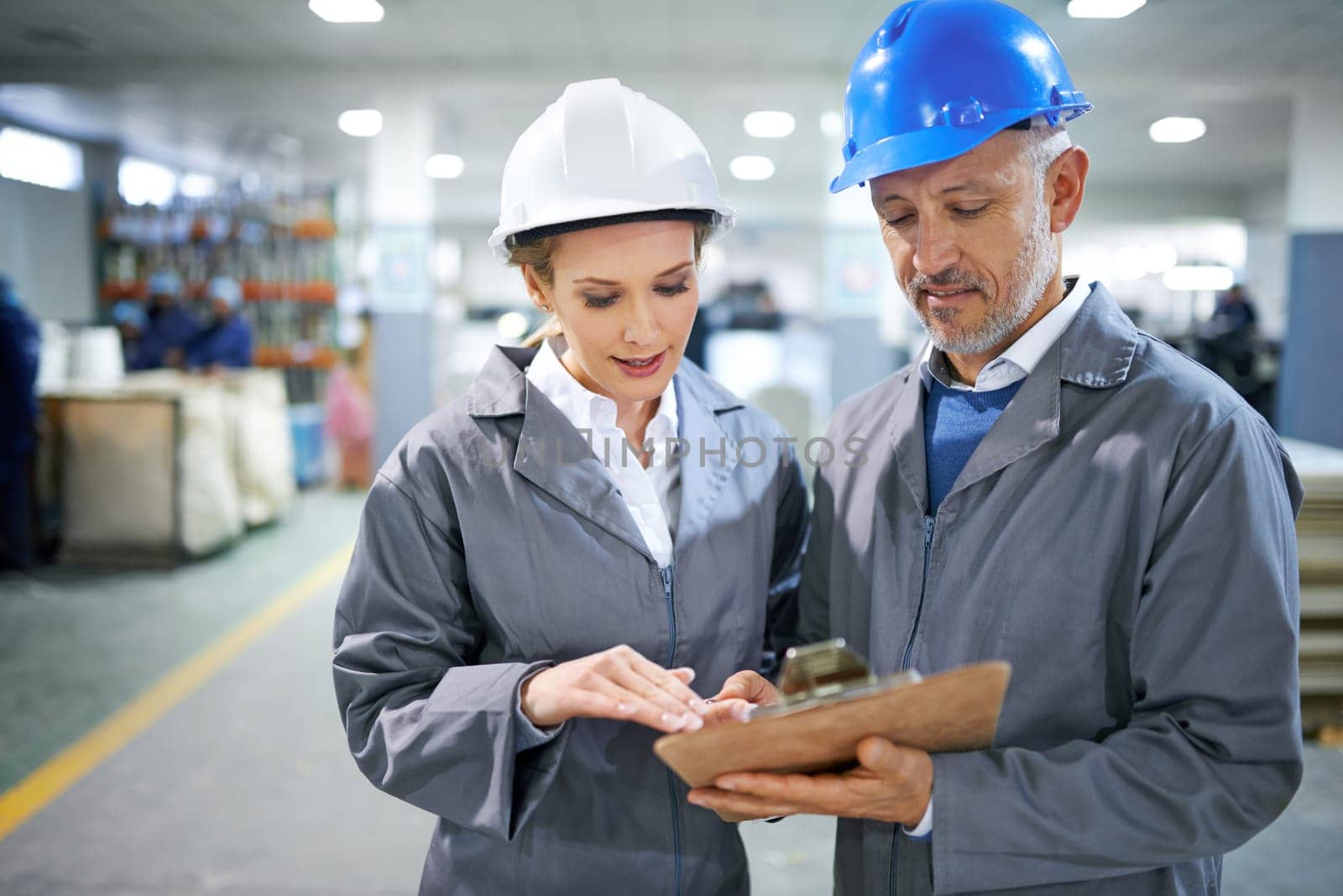 Man, woman and conversation with clipboard in factory for quality inspection or safety checks and process monitoring. Team, communication and board for manufacturing information in printing warehouse.