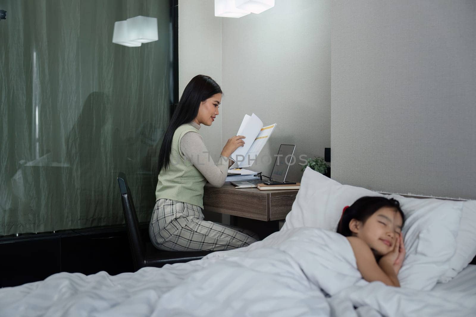mother work late into the night after putting her child to sleep in the bedroom by itchaznong