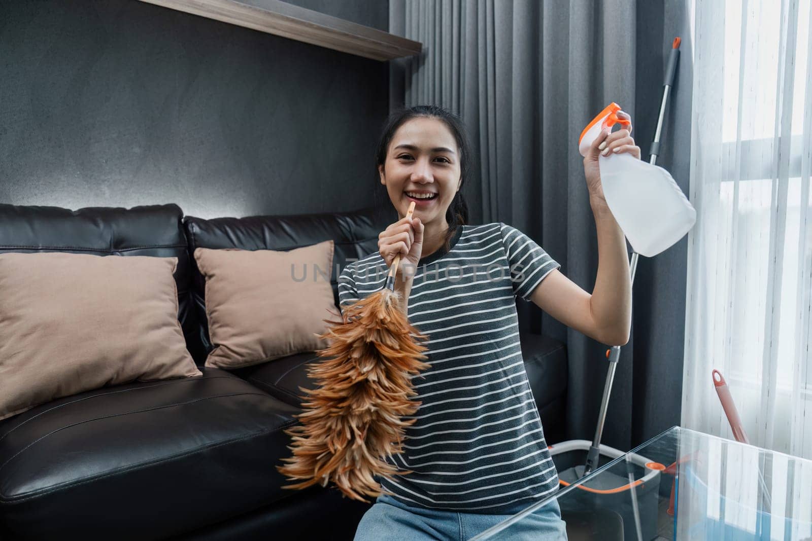 Asian woman happily use feather pick as microphone while cleaning house on the weekend by itchaznong