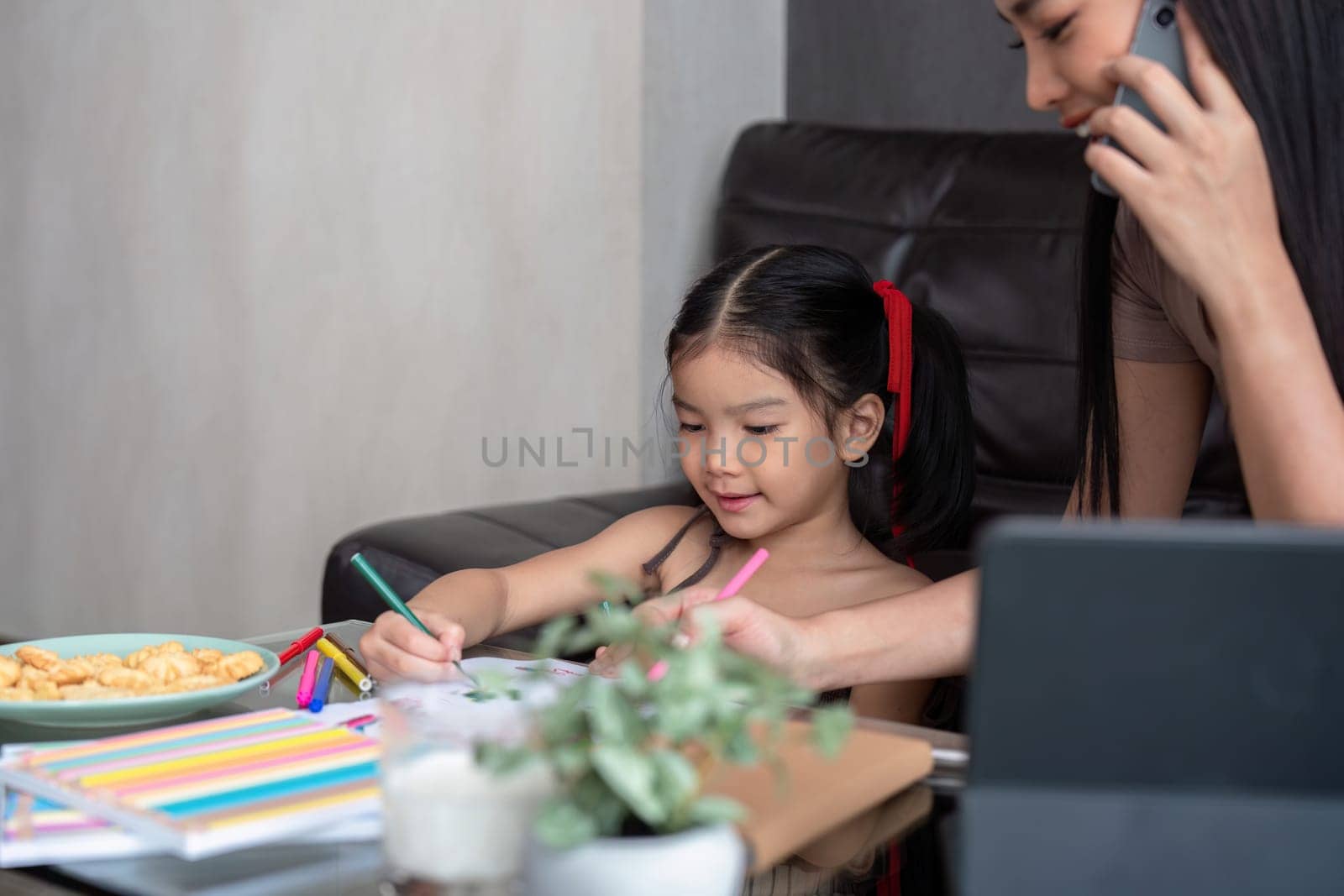 Working mother concept. Young woman working on laptop with her child from home.