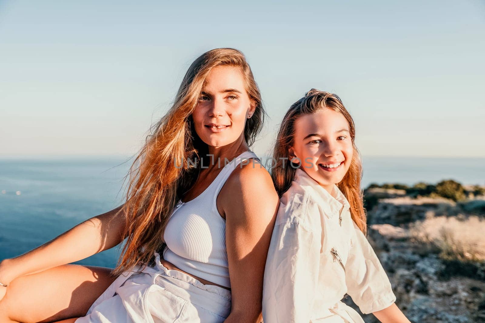 Close up portrait of mom and her teenage daughter hugging and smiling together over sunset sea view. Beautiful woman relaxing with her child.